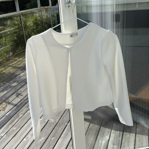 Vit croppad kofta från C - Snygg vit kofta från C med croppad passform och rund halsringning. Långärmad och enkel design utan knappar eller dragkedja, perfekt att slänga över en topp. Mjukt material som känns bekvämt mot huden.