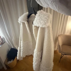 Vit teddyjacka från Maje, stl 36 - Säljer en superfin vit teddyjacka från Maje i storlek 36. Jackan har fluffig krage och detaljer vid ärmslut och nederkant, samt knappar framtill. Perfekt för dig som vill ha en mysig och trendig look under kyliga dagar.