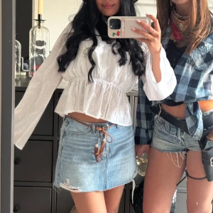 Vit blus med broderade detaljer - Superfin vit blus med v-ringning och broderade hålmönster. Blusen har långa, vida ärmar och markerad midja med volang nedtill. Det ärver lite uppet i ryggen längst upp som man kan knyta! Använd ett fåtal gånger så i mycket bra skick🤩