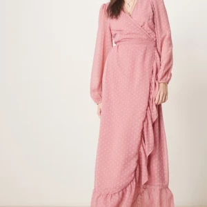 Rosa omlottklänning från Vila - Rosa omlottklänning från Vila med prickigt mönster, volangkant nertill och långa ärmar. Klänningen har v-ringning och knyt i midjan för en snygg passform. Helt ny med prislappar kvar! 