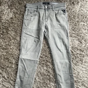 Grå Replay Anbass - Grå jeans från Replay, modell Anbass med slim fit passform. W31 L30.. Bra skick förutom litet hål vid skrevet som förmodligen är enkelt att laga. Skriv vid frågor