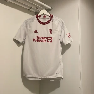 Manchester United vit bortatröja Adidas - Säljer en vit Manchester United bortatröja från Adidas med röda detaljer och loggor. TeamViewer och DXC Technology tryck på bröst och ärm. Tvär så att hitta köpte den för 1,4 säljer för 500 hör av dig vid minsta funderingar  S/ passar och M