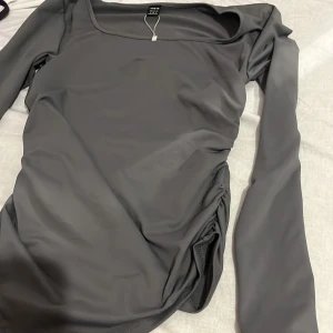 Grå långärmad topp från SHEIN - Säljer en stilren grå långärmad topp från SHEIN i storlek S. Toppen har en snygg, fyrkantig ringning och är gjord i ett stretchigt, slätt syntetmaterial som sitter tight mot kroppen. Perfekt att matcha med jeans eller kjol för en clean look.