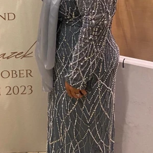 Glittrig långklänning i silver - Snygg långklänning i silver med glittriga pärldetaljer och långärmad design. Klänningen har ett elegant mönster av pärlor som ger en lyxig känsla och passar perfekt för speciella tillfällen.