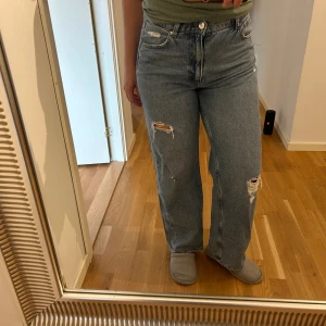 Blåa wide jeans med slitningar - Säljer ett par blåa jeans med bred passform och snygga slitningar på båda benen.