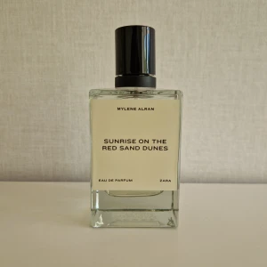 Zara Sunrise on the Red Sand Dunes - Parfymen Sunrise on the Red Sand Dunes från Zara har en stilren, rektangulär glasflaska med svart lock. Doften är skapad av Mylene Alran och är en Eau de Parfum. Flaskan är transparent med ljusgul vätska och minimalistisk etikett.