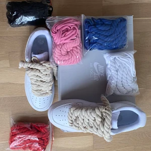 Nike Air Force 1 med chunky snören - Unika vita Nike Air Force 1 sneakers med extra chunky snören i flera färger: beige, svart, rosa, blå, vit och röd. Klassisk låg modell i skinn med perforerad tå och platt sula. Perfekt för dig som vill sticka ut med en personlig touch.