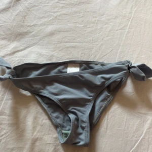 Grå bikiniunderdel från Surfin Skill - Snygg grå bikiniunderdel från Surfin Skill med knyt i sidorna för en cool och justerbar passform. Perfekt för strandhäng och poolparty. Materialet är mjukt och följsamt syntet som torkar snabbt. Enkel design som är lätt att matcha med olika överdelar.