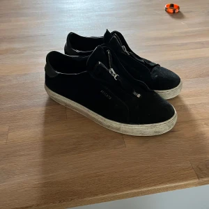 Svarta sneakers från Axel Arigato - Svarta sneakers från Axel Arigato med snygg dragkedjedetalj på ovansidan. Skorna har en platt vit sula och är tillverkade i mocka och skinn. Har inte tvättat dom än men om man gör de så kommer dom se ut som nya vid snabb affär kan jag tänka mig o gå ner i pris säljs inte på axel arigatos hemsida längre hör av vid minsta lilla!