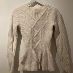 Vit stickad tröja från Ted Baker - Supersnygg vit/beige stickad tröja från Ted Baker med figurnära passform och peplumdetalj nedtill. Tröjan har ett unikt stickat mönster framtill och långa ärmar. Perfekt för dig som gillar stilrena och trendiga plagg med det lilla extra.