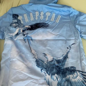 Trapstar  vindjacka. Storlek S - Säljer min äkta Trapstar jacka i storlek S. Jackan är i fint skick och har en snygg design med örnar på ryggen och “Trapstar”-loggan. Tyvärr blev den för liten för mig, därför säljer jag den vidare. Kan diskutera om pris !! 