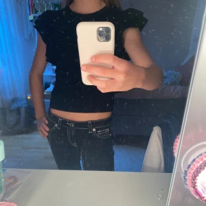 Svart volangblus från Gina Tricot - Supersnygg svart blus från Gina Tricot med volangdetaljer på axlarna och ribbad struktur.  Materialet är mjukt och stretchigt, vilket gör den bekväm att bära hela dagen. Använd 1-2 gånger❣️❣️