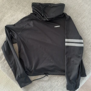 Svart träningströja från Stronger med snörning - Svart tjockare tröja från Stronger med hög krage och snörning vid krage och nederkant. Är i storleken s, tröjan är i bra skick 