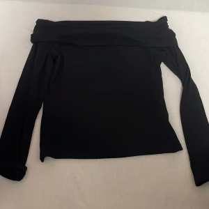 Svart offshoulder topp från 157 - Svart långärmad offshoulder topp från 157. Snygg och enkel design med bred kant upptill som ger en stilren look. Perfekt att styla med jeans eller kjol för en trendig outfit. Mjuk och stretchig känsla.