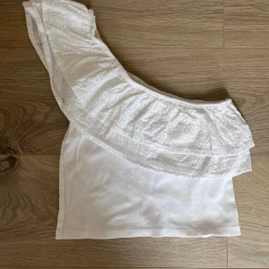 Vit oneshoulder topp med volang 146/152 - Vit, kort ribbad topp med en bar axel och volang med broderier.  Vit topp one shoulder Gina Tricot Young 146/152  Toppskick