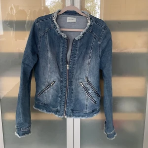 Jeansjacka från Pimkie med dragkedjor - Snygg blå jeansjacka från Pimkie med fransade kanter vid hals, ärmslut och nederkant. Jackan har två snedställda fickor med dragkedjor och stängs med dragkedja framtill. Klassisk passform och cool denim-look som passar till allt. Skriv om du undrar något 💞jag skulle tro att storleken är S/M 