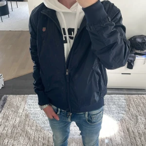 Morris marinblå vindjacka herr - Snygg marinblå vindjacka från Morris med klassisk passform. Perfekt nu när de börjar bli lite kallare, men även perfekt till våren! Nypris ca 1800kr, mitt pris 799kr! Modellen är ca 180cm. Hör av dig vid funderingar!