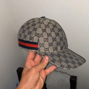 Gg keps  - Snygg keps från gg med klassiskt GG-monogram över hela kepsen och en ikonisk röd-blå rand på sidan. Beige bas med mörkblå detaljer, böjd skärm och justerbar passform. Perfekt för dig som vill sticka ut med en lyxig accessoar. Pris jag kan diskuteras vid snabb affär