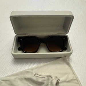 Bruna solglasögon från CHIMI - Snygga solglasögon från CHIMI i mörkbrunt med fyrkantig form och bruna tonade glas. Kommer med originaletui i beige. Perfekta för att lyfta din stil under soliga dagar. Köpte för 1400kr