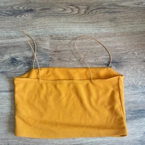 Gul bandeau tubtopp med tunna band - Snygg gul bandeau tubtopp med tunna axelband. Enkel och stilren design, perfekt för varma dagar. Toppen är croppad och har en rak passform. Tillverkad i mjukt bomullsmaterial som känns skönt mot huden.