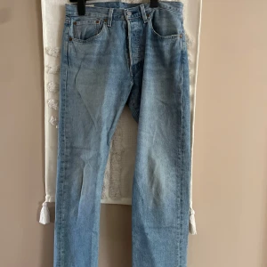 Levi's 501 ljusblå jeans W31 L32 - Klassiska Levi's 501 jeans i ljusblå tvätt. Rak passform med fem fickor, knappgylf och ikonisk röd Levi's-tag på bakfickan. Tillverkade i slitstarkt bomullsjeans, perfekta för en avslappnad och tidlös look.