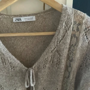 Beige kofta från Zara - Supersöt beige stickad kofta från Zara med v-ringning, knyt framtill och spetsdetaljer längs axlarna. Koftan har ett fint hålmönster, volangkant nertill och långa ärmar. Perfekt för lager-på-lager. Tröjan är köpt i Rom för ett halvår sedan men har knappt använts sedan dess och är i fint skick. Storleken är medium och nypris ligger kring 500 men jag säljer för 300 men priset är dock inte hugget i sten och jag är beredd att förhandla