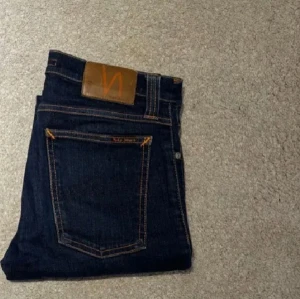  Nudie Jeans - Säljer ett par mörkblå jeans från Nudie Jeans med klassisk femficksdesign och snygga kontrastsömmar. Storlek 27/32. Skick 10/10