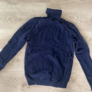 Mörkblå polotröja i ull - Mysig mörkblå polotröja med lång ärm och ribbade muddar. Perfekt för kyliga dagar och enkel att matcha med jeans eller kjol. Tillverkad i mjuk ull som håller dig varm och bekväm hela dagen.