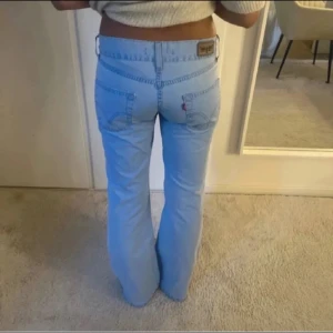  ljusblå bootcut byxor - Snygga ljusblå byxor med bootcut passform och låg midja. Klassisk femficksmodell med detaljerade sömmar och logga på bakfickan. Tillverkade i mjuk bomull för en skön känsla. Perfekta för dig som gillar retrovibbar och relaxed stil.