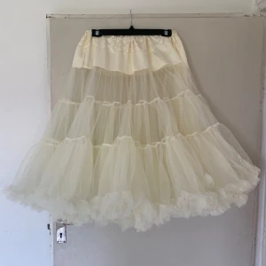 Voluminös vit tyllkjol från Hell Bunny - Superfin underkjol i vit tyll från Hell Bunny. Kjolen har flera lager volanger som ger en riktigt fluffig och dramatisk look. Perfekt för dig som vill sticka ut med en maxad och romantisk stil. Resår i midjan för skön passform.