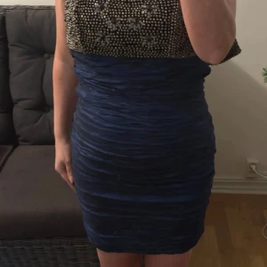 Blå axelbandslös klänning Sorbet - Snygg blå axelbandslös kortklänning från Sorbel med glittrig pärlbroderad överdel och draperad kjol. Klänningen har en figurnära passform och stängs med dragkedja bak. Inga axelband, sitter uppe med gummiband. Storlek L men upplever den som en S/M. Ev kan ngn pärla ha lossnat men inget som syns direkt.