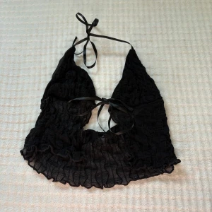 Svart omlott halterneck topp Shein - Säljer en svart halterneck topp från Shein i storlek XS. Toppen har omlottknytning i nacken och vid bysten, är ärmlös och har ett transparent, vågigt mesh-tyg med snygg struktur. Perfekt för dig som gillar trendiga och unika detaljer.