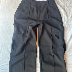 Svarta kostymbyxor  - Säljer mina Svarta kostymbyxor från Gina Tricot med raka ben och stora sidofickor. Med knapp och dragkedja. Snygg look med lite loose fit. Säljer pågrund av att dem inte kommer till användning 