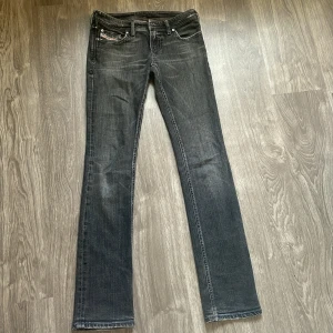 Svarta/grå Diesel jeans  - Snygga svarta jeans från Diesel med diskret tvättad look och raka ben. Klassisk femficksmodell med tydliga Diesel Industry-detaljer och broderad logga på bakfickan. Jeansen har normal passform och är tillverkade i slitstarkt denim. Dem är ungefär 40cm tvärs över midjan. Innerbenslängden är ungefär 84cm. 