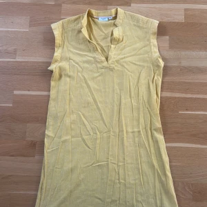 Gul ärmlös linne klänning från Saint tropez - Snygg gul klänning från Saint med v-ringning och ärmlös design. Lätt och luftig modell i bomull, perfekt för varma dagar. Enkel men stilren look som passar dig som gillar färg och vill sticka ut lite extra.
