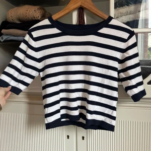 Randig stickad tröja med trekvartsärm - Snygg stickad tröja med marinblå och vita ränder. Tröjan har trekvartsärm och rund halsringning med marinblå kant. Perfekt för en chill och stilren look, passar till både jeans och kjol.