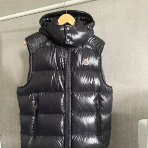 Svart dunväst från Moncler med huva - Säljer en svart, glansig dunväst från Moncler med avtagbar huva och dragkedja framtill. Inga skador på västen. Västen är som ny.                                                 Skriv för mer information och bilder!