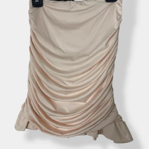 Champagnefärgad kjol med topp - Supersöt set i champagnefärgad med tunna axelband. Kjolen har snygga rynkade detaljer framtill och volang längst ner. Perfekt för dig som gillar en feminin och trendig look med lite extra volym.