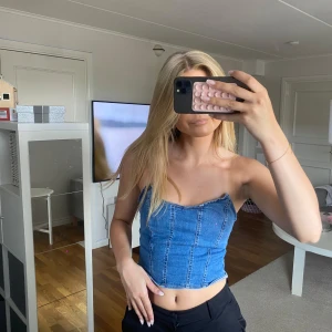 Jeans korsettopp från NA-KD - Säljer en snygg croppad jeans korsettopp från NA-KD i klassisk blå denim. Toppen är axelbandslös med markerade sömmar framtill.