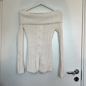 Offshoulder ribbad kofta i vitt - Superfin offshoulder ribbstickad tröja. Långärmad modell med knappar framtill och bred, nedvikt krage. Aldrig använd men har provat på. Köpt från okänt märke på Yesstyle.