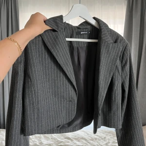 Grå randig kavaj från Gina Tricot - Snygg grå kavaj från Gina Tricot i croppad modell med smala vita ränder. Tunnare material som känns bekvämt och passar till många outfits. 