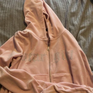 Rosa velour hoodie från Newyorker - Säljer en ljusrosa hoodie i mjuk velour. Jackan har huva, dragkedja och fickor framtill. På bröstet står det 'star girl' i glittriga stenar som ger en extra cool vibe. Perfekt för dig som gillar comfy och trendigt.