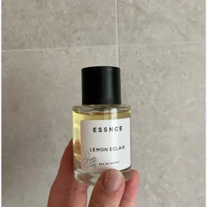 ESSNCE Lemon Eclair parfym - Fräsch parfym från ESSNCE med doften Lemon Eclair. Kommer i en stilren, rund glasflaska med svart lock och vit etikett. Parfymen har en ljusgul vätska och är en Eau de Parfum. Perfekt för dig som gillar citrusdofter.