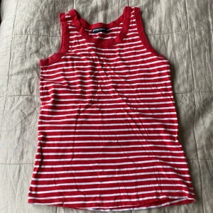 Rödvit randig linnetopp Point Zero - Säljer en snygg röd och vit randig linnetopp från Point Zero i storlek 40. Toppen är ärmlös med klassisk rund halsringning och smala axelband. Perfekt för varma dagar och enkel att matcha med jeans eller shorts.