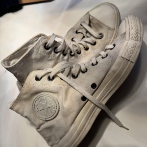 Vita Converse All Star high-top sneakers - Klassiska vita Converse All Star high-top sneakers i canvas med rund tå och snörning. Skorna har den ikoniska logotypen på sidan och gummisula med mönstrad tå. Perfekta för en avslappnad och cool streetstil. Söndriga i hälen. 