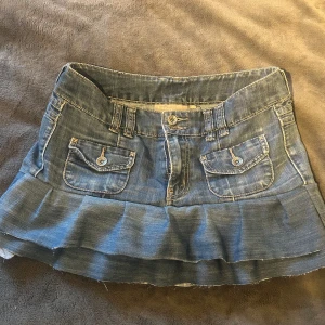 Blå jeanskjol med volang. - Supersöt blå jeanskjol med volang nertill och snygga fickor fram och bak. Kjolen har bälteshällor, knappar och dragkedja.💘 Den är egensydd!