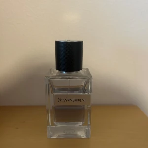 Yves Saint Laurent Y EDT 60ml - Snygg parfym från Yves Saint Laurent i en stilren, fyrkantig glasflaska med svart, räfflad kork. Flaskan är transparent och visar den ljusa vätskan inuti. Märkets logga sitter på en metallplatta framtill. Perfekt för dig som gillar exklusiva dofter. KÖP ELLER BYT!