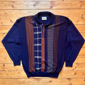 Retro stickad pikétröja från Marcello - Säljer en retro stickad pikétröja från Marcello i marinblått och brunt med unika mönstrade paneler framtill. Tröjan har krage, knappar vid halsen och långa ärmar. Perfekt för dig som gillar vintagevibbar och coola detaljer.