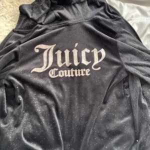 Juicy Couture svart glittrig hoodie XS - Svart hoodie från Juicy Couture med glittriga detaljer och stor logga på ryggen. Mjuk och stretchig i polyesterblandning, dragkedja framtill och huva. Perfekt för dig som vill ha en ikonisk och trendig look.