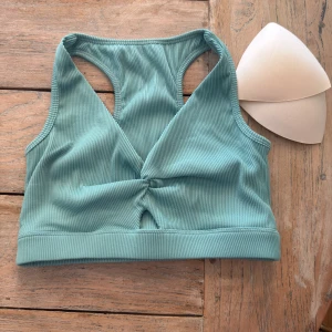 Ribbad grön sporttopp Workout Empire - Sporttopp från Workout Empire i ribbad, ljusgrön polyester. Modellen har brottarrygg, uttagbara inlägg och en snygg twist-detalj framtill. Perfekt för träning och ger bra stöd. Broderad logga framtill på resåren. Ilägg om du vill ha ett lyft.